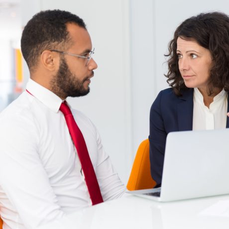 Man and woman sitting at conference table with laptop, talking